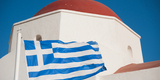 Sky_blue-white_(flag_of_Greece)_against_the_background_of_the_Monastery_of_Panagia_Tourliani._Mykonos_island,_Cyclades,_Agean_Sea,_Greece